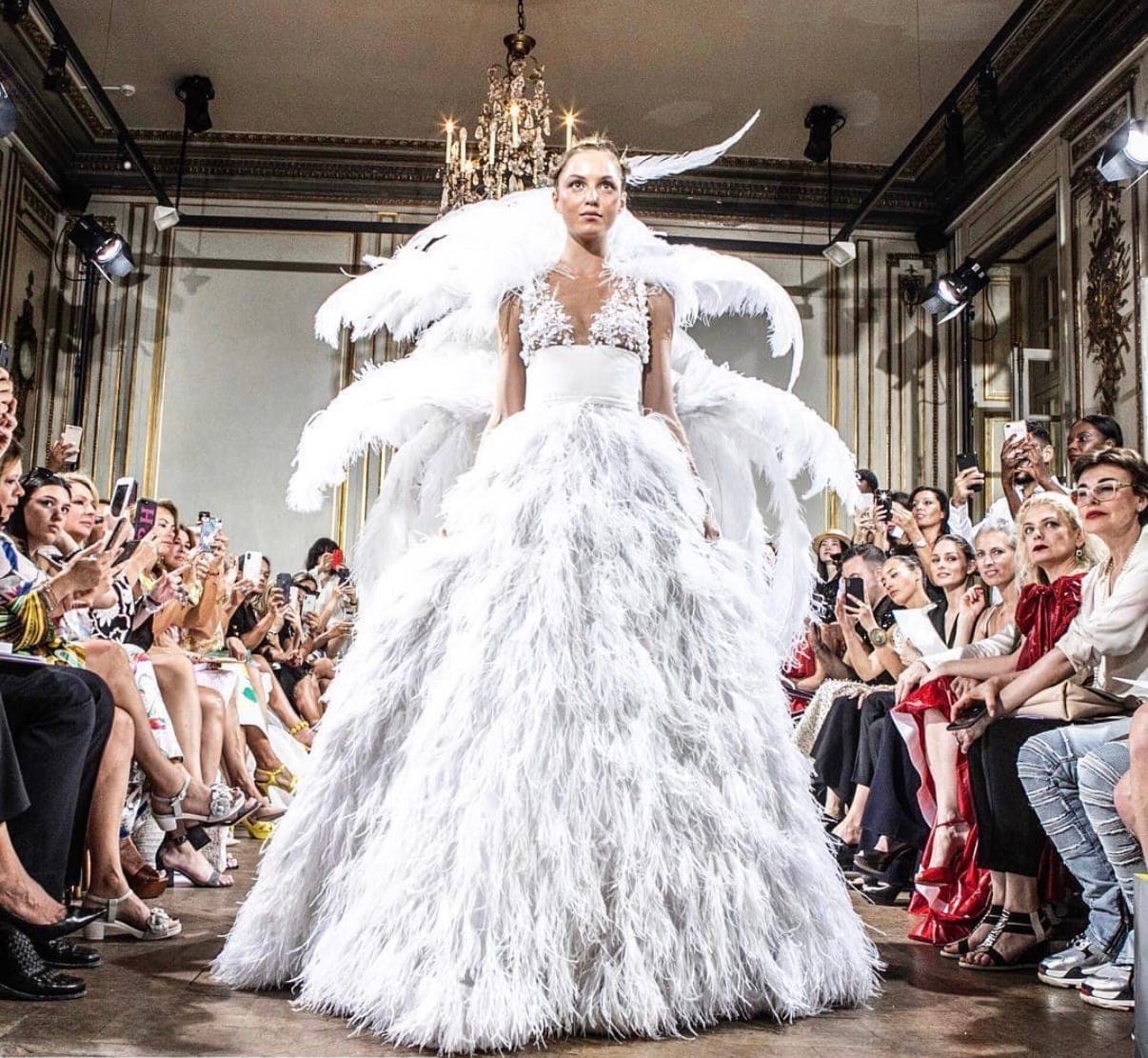 A couture runway show — a model in a feathered white gown